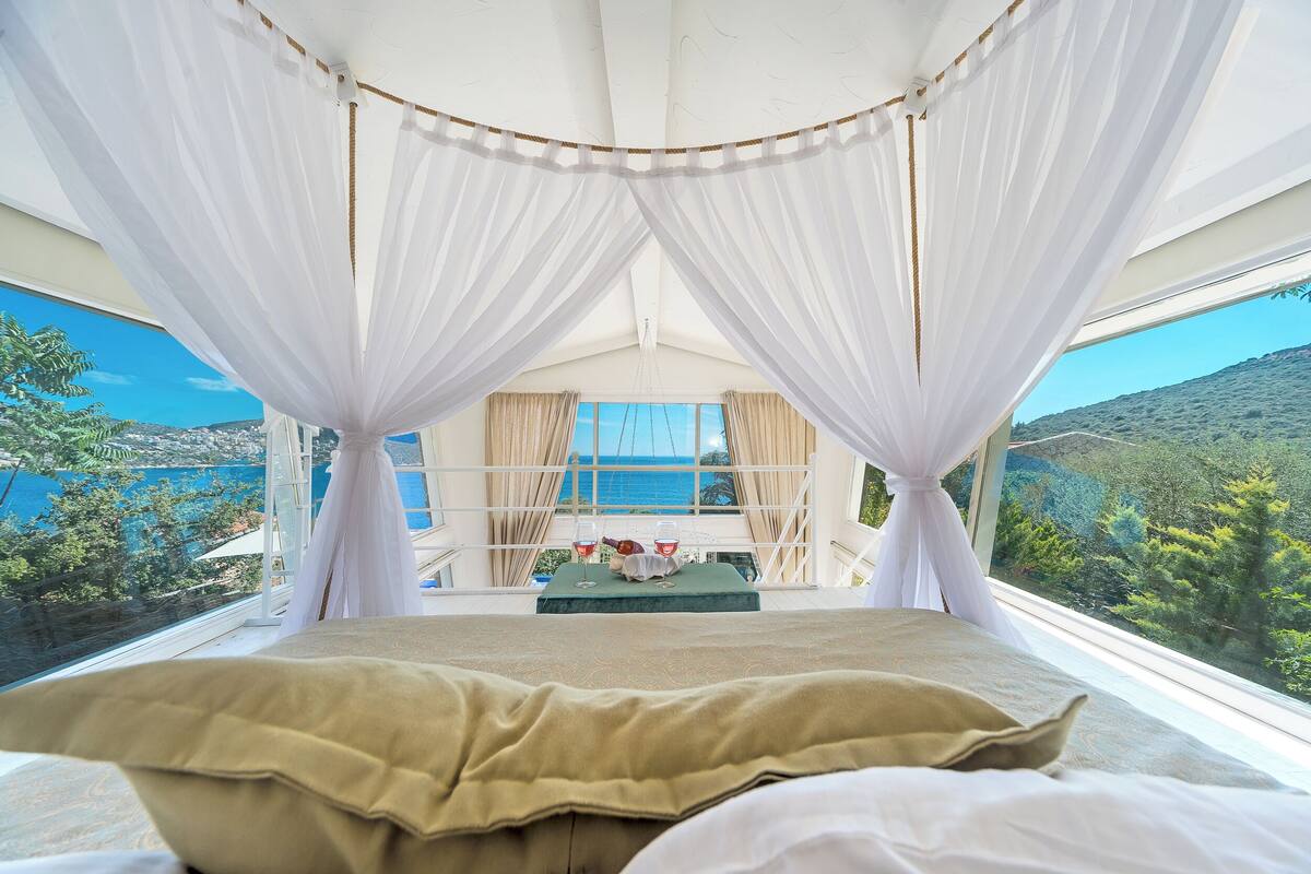 A room with a bed, curtains, and a view of the sea.