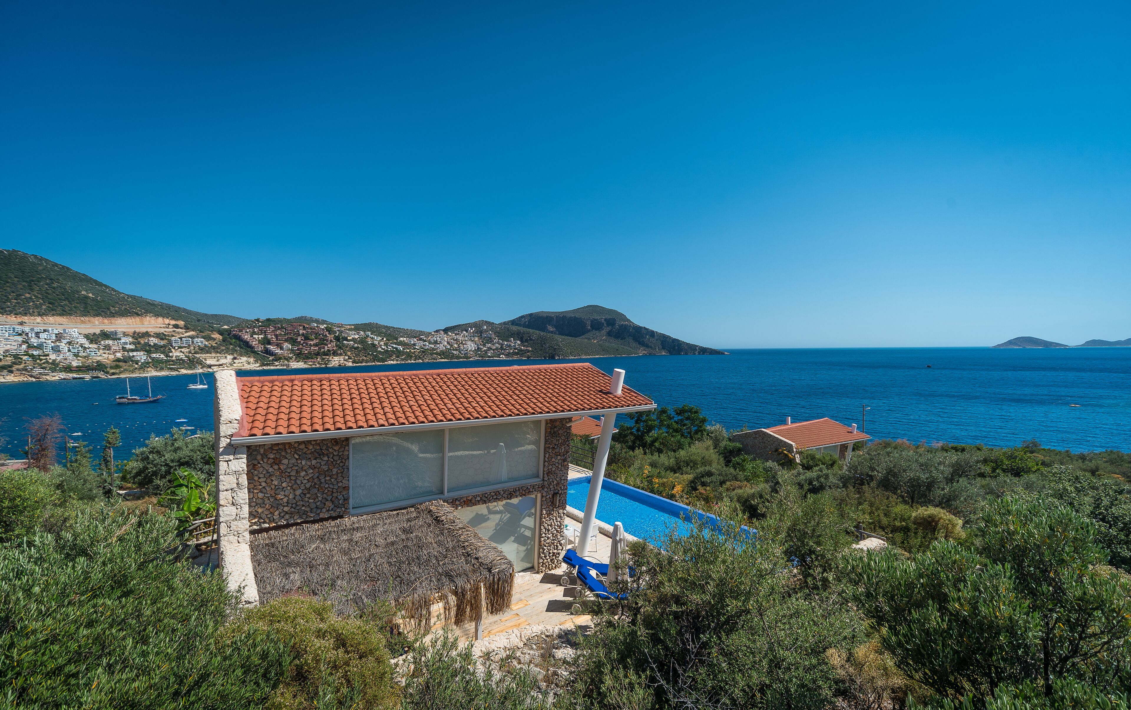 Eine Küstenvilla mit Swimmingpool, Blick auf das Meer und einer Stadt am Hang im Hintergrund.