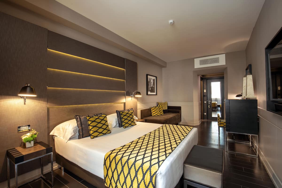 A modern hotel room with a large bed, bedside tables, a desk, and a television.