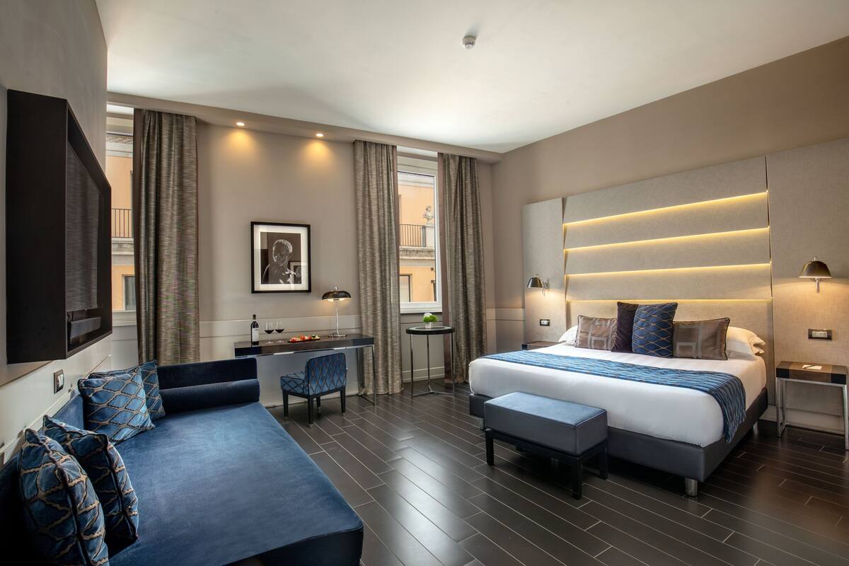 A modern hotel room with a large bed, a sofa, a desk, and a TV.