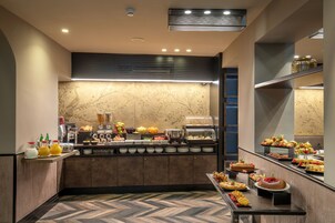 A buffet with various food items, a coffee station, and a fruit display.