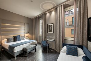 A modern hotel room with a large bed, a smaller bed, a desk, and a view of the city.