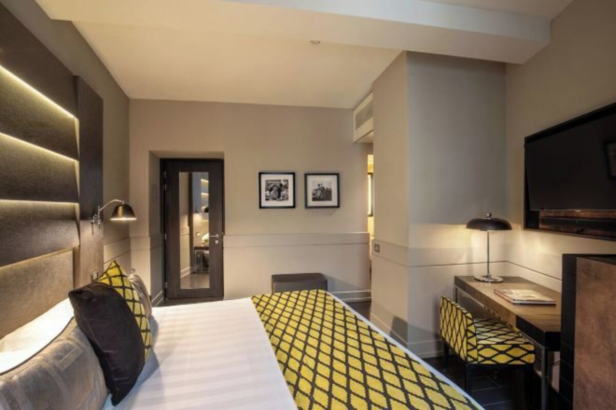 Une chambre d’hôtel avec un lit, un bureau, une chaise, une télévision et des tableaux encadrés au mur.