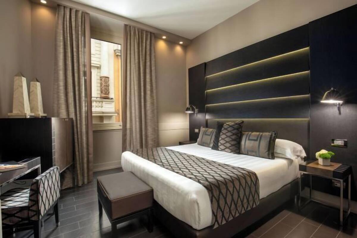 A modern hotel room with a large bed, a desk, and a chair.