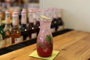 Un cóctel en un vaso sobre una barra de madera con botellas al fondo.