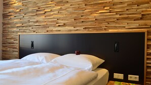 A neatly made bed with white linens, a wooden headboard, and a small bedside table with a book and a power outlet. - Hotel FIVE (Nuremberg)