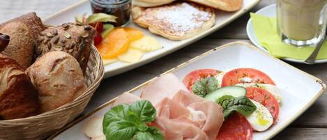 A breakfast setting with bread, pancakes, and a plate of salami, prosciutto, and eggs.