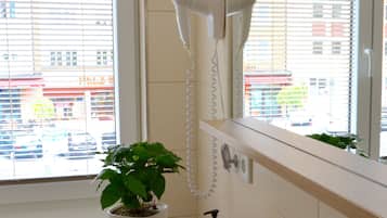 A bathroom with a hairdryer mounted on the wall, a potted plant, and a bottle of lotion.