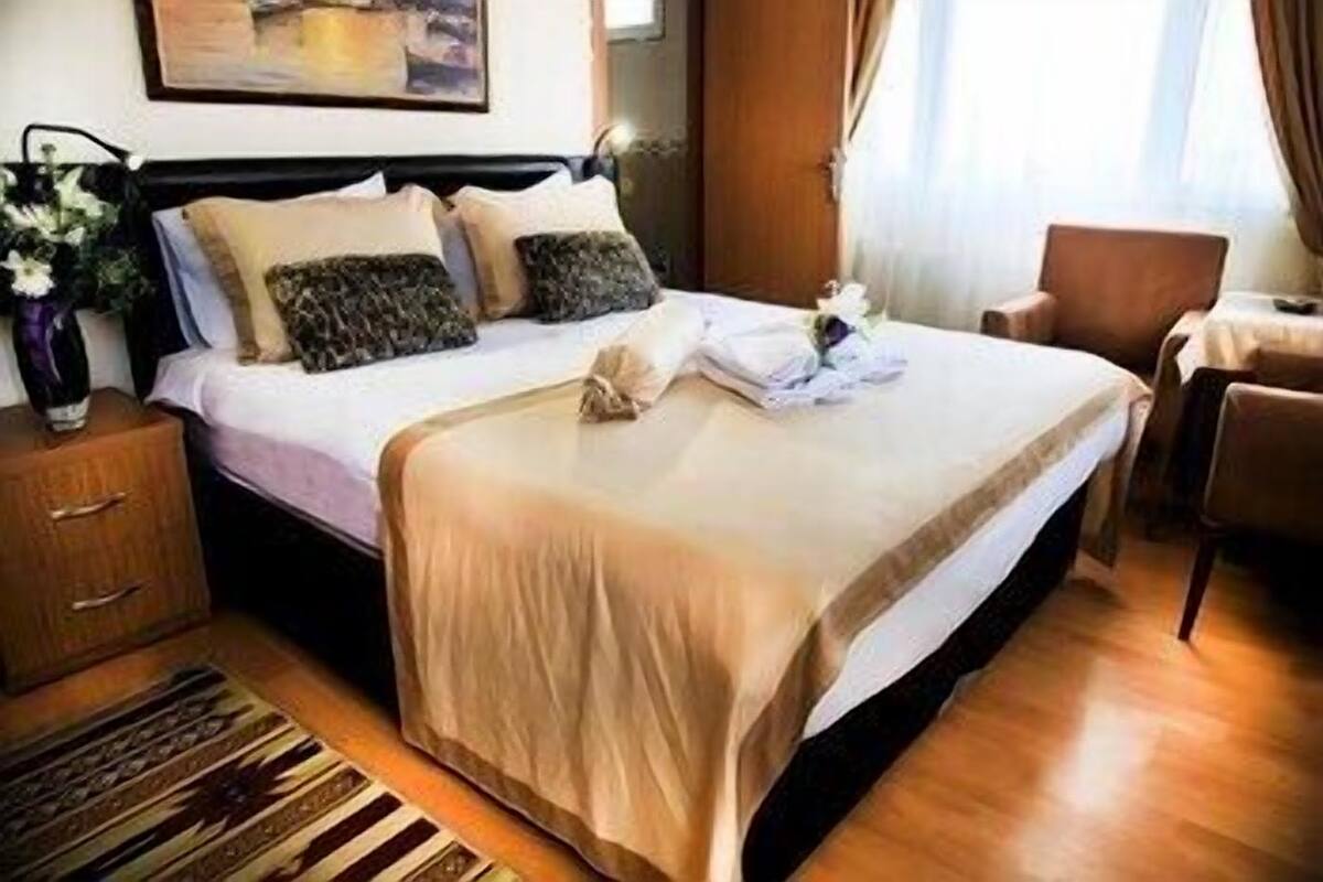 Una habitación de hotel con cama, mesita de noche, una silla y ventana con cortinas.