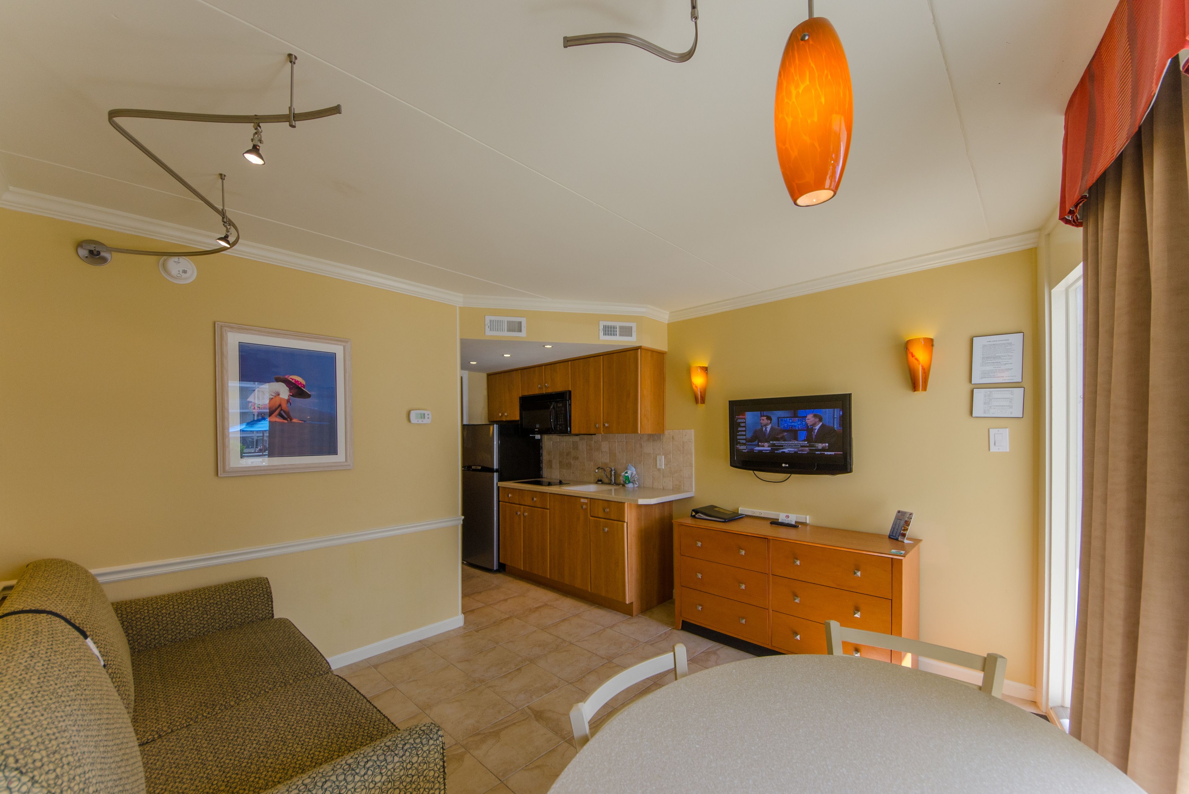 A hotel room with a kitchenette, a dining area, a TV, and a sofa.