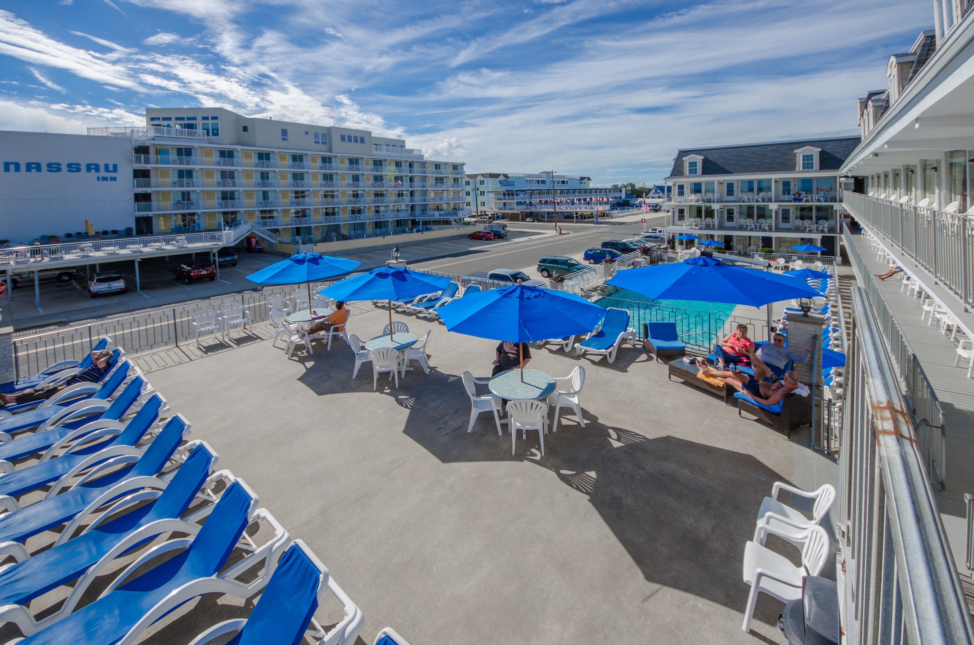 A beachfront hotel with outdoor seating areas, multiple balconies, and a parking lot.