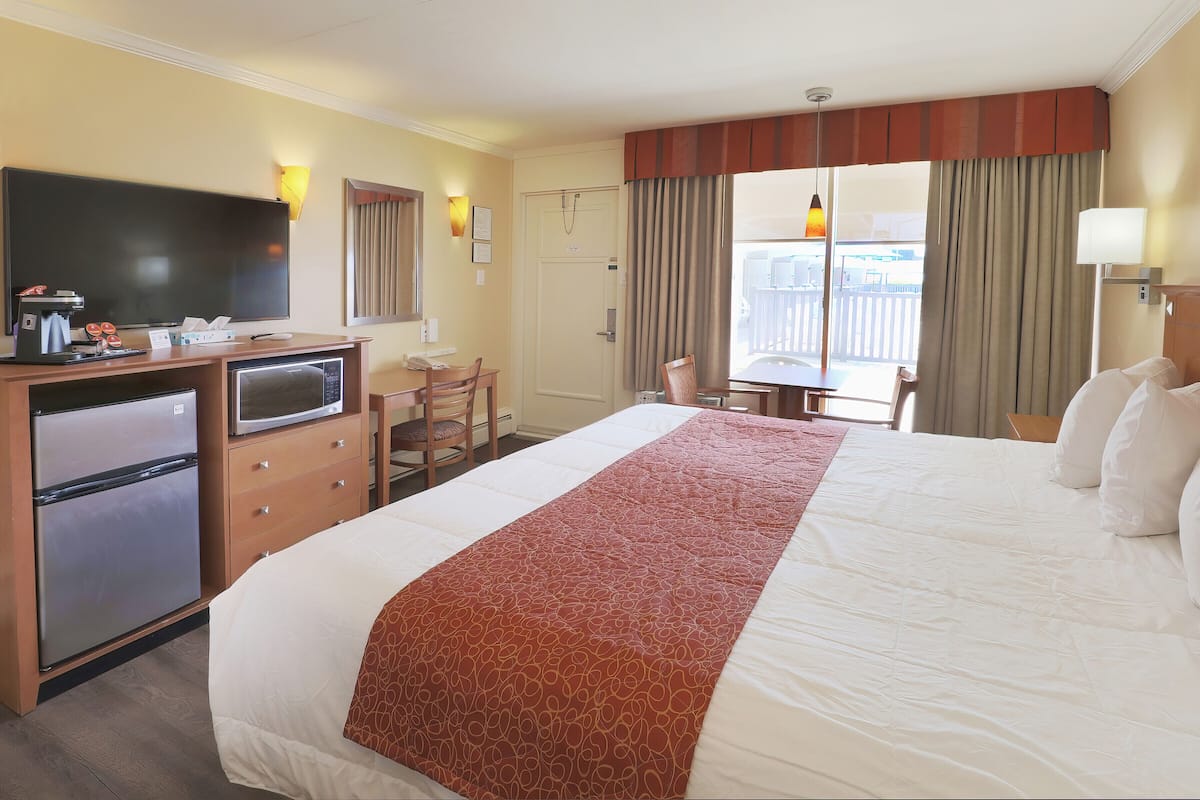 A hotel room with a large bed, a desk with a chair, a television, a minibar, and a window with curtains.