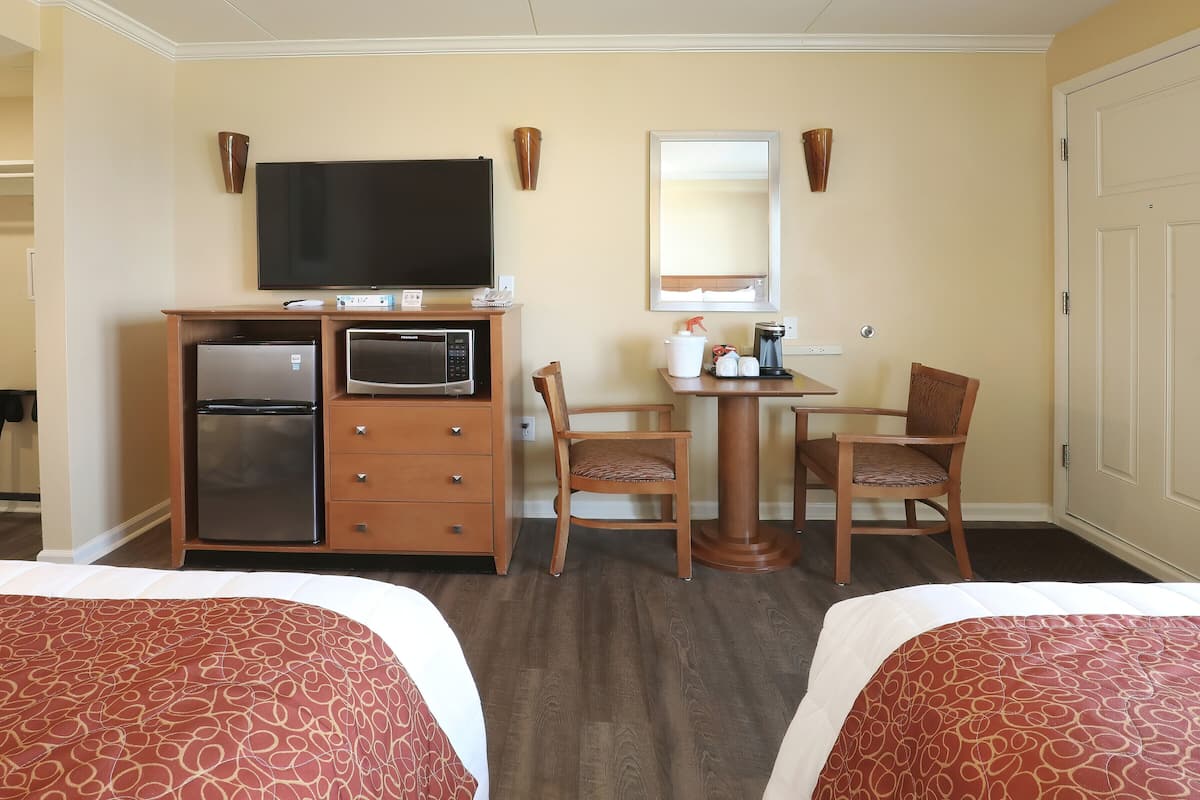 A hotel room with two beds, a desk with a chair, a refrigerator, a microwave, a television, and a mirror.