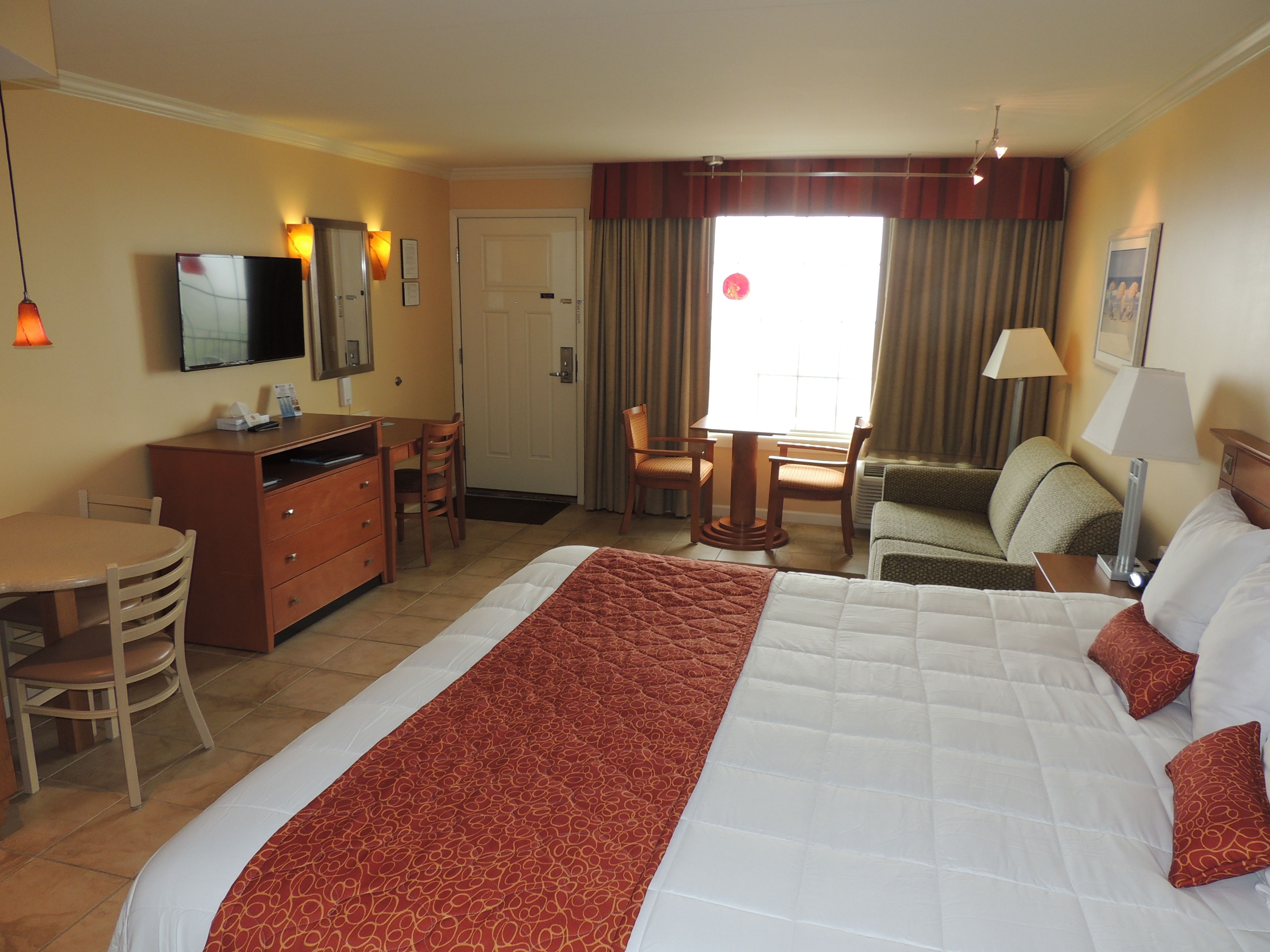 Une chambre d’hôtel avec un grand lit, un bureau, une chaise, une télévision et une fenêtre avec des rideaux.