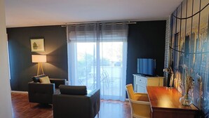 Habitación de hotel con cama, escritorio, sillón, sofá, lámpara y vistas al exterior.