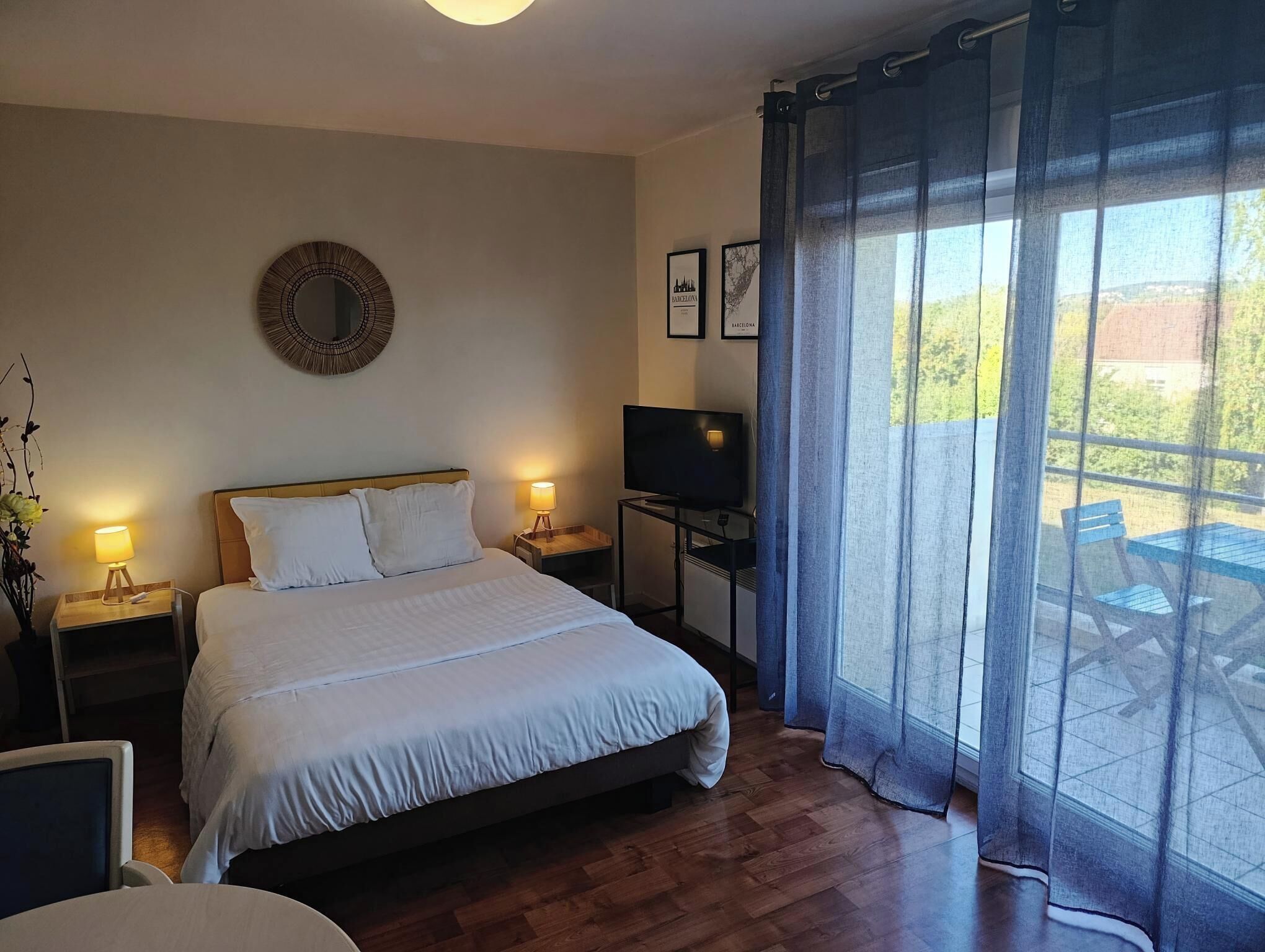 A bedroom with a bed, bedside lamps, a TV, a mirror, and a view of the outdoors.