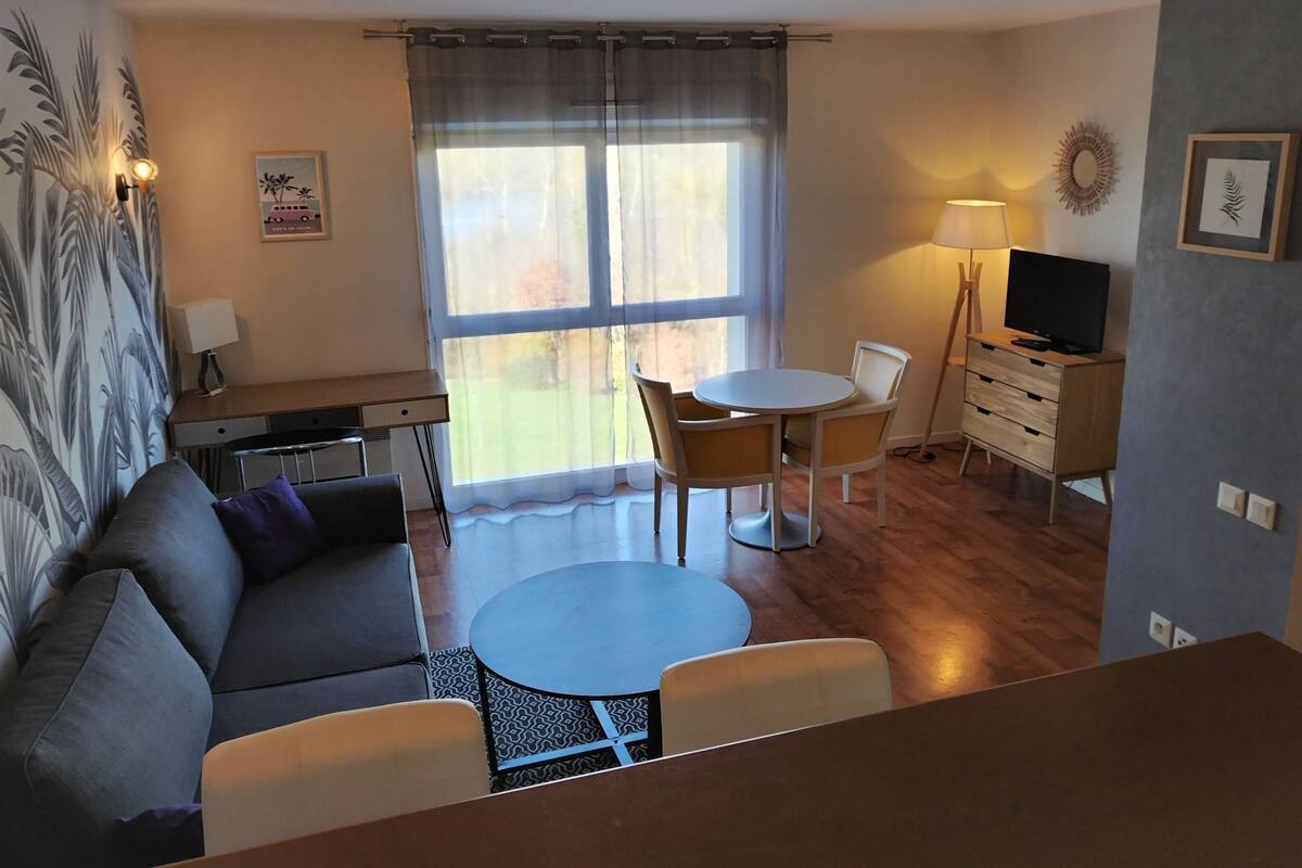 A compact living space with a sofa, a small round table, a TV stand, and a dining area.