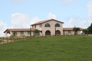 A two-story building with a flat roof, arched windows, and a fenced property. - Pietriccio Rosso (Manciano)