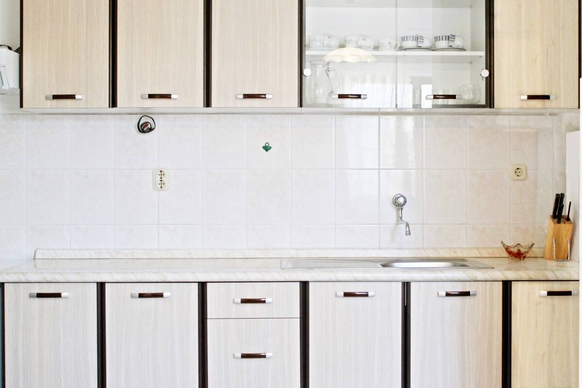 Cozinha moderna com armários de madeira clara, painel de azulejos branco e pia de aço inoxidável.