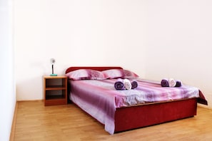A neatly made bed with a red headboard and a purple and pink bedspread, accompanied by two rolled towels and a small bedside table with a lamp. - Villa Brksi (Split)