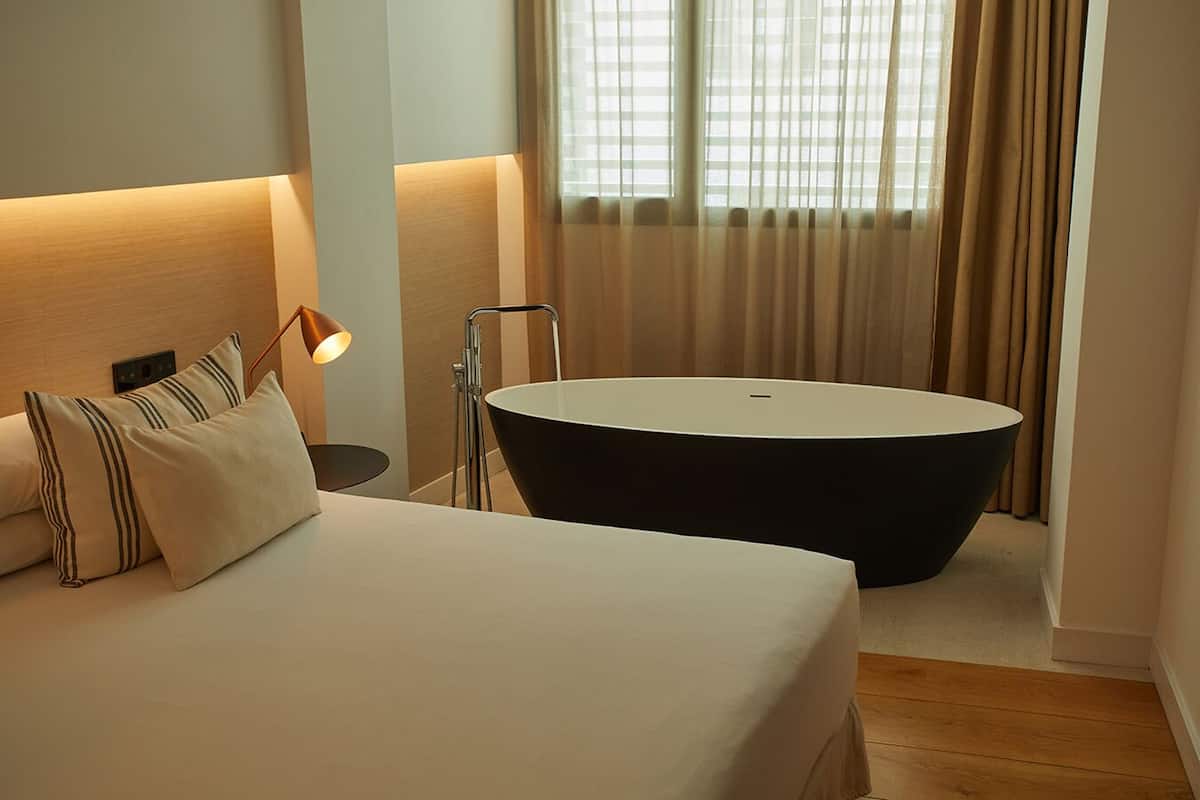 Een moderne hotelkamer met een groot bed, een zwart bad en een bedlamp.