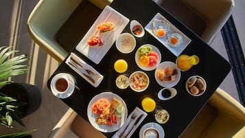Een gedekte tafel met diverse ontbijtartikelen, zoals eieren, fruit en gebak, en stoelen eromheen.