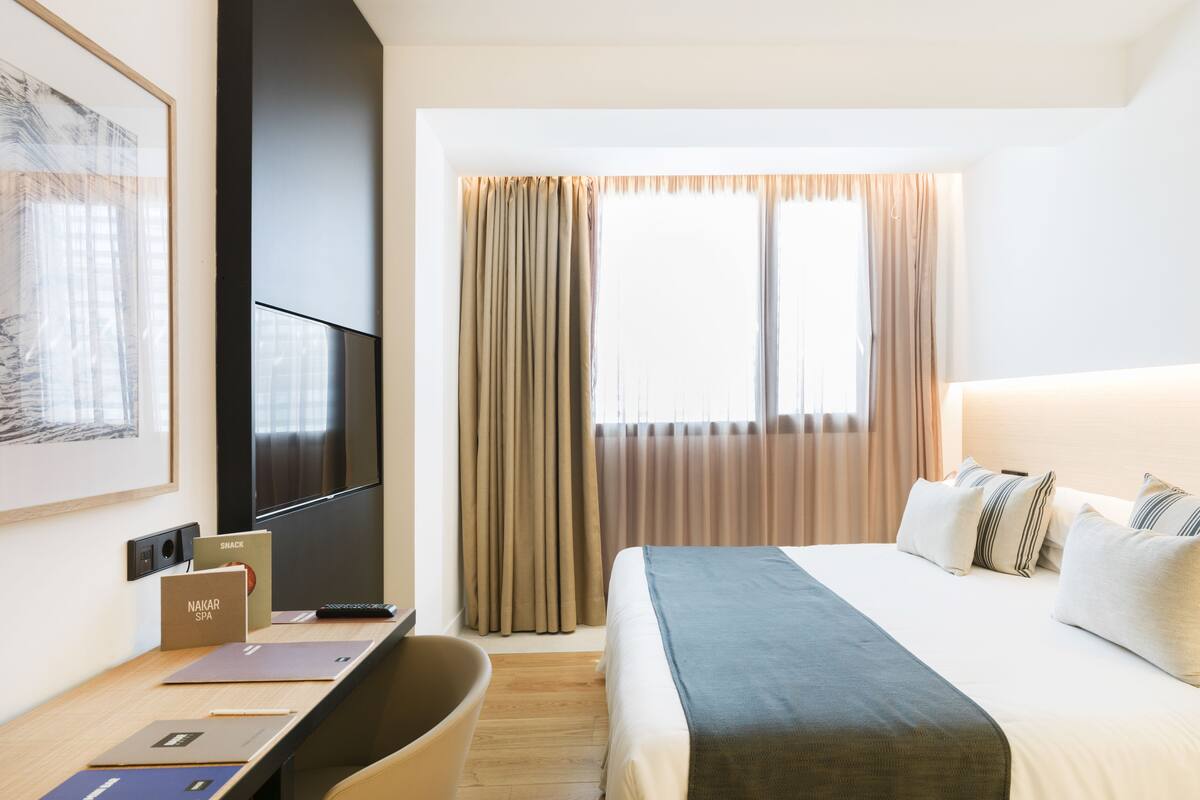 Een hotelkamer met een bed, een bureau met een laptop, een televisie en een raam met gordijnen.