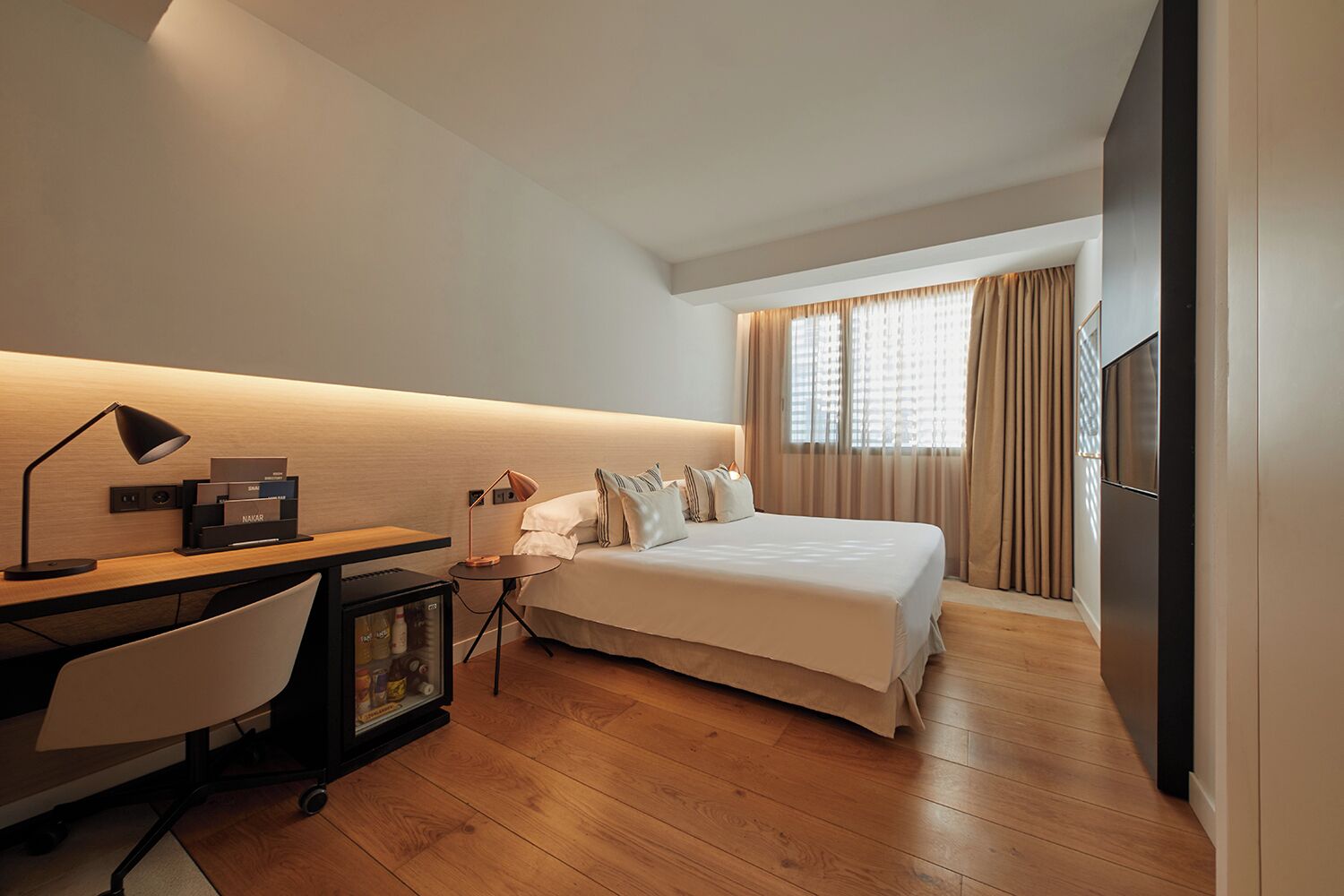 A hotel room with a bed, desk, chair, and a minibar.