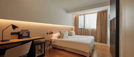 A hotel room with a bed, desk, chair, and a minibar.