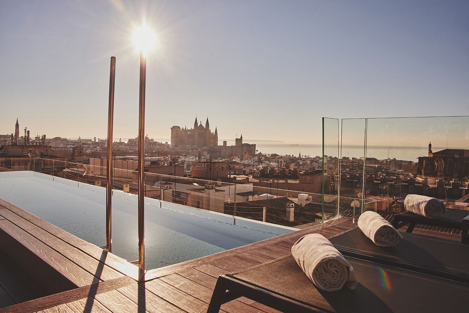 Una piscina en la azotea con vista a la ciudad, una terraza de madera y un espejo grande que refleja el entorno.