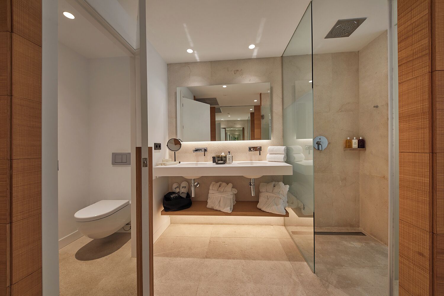 A modern bathroom with a glass shower enclosure, a white toilet, and a vanity with a mirror and multiple sinks.