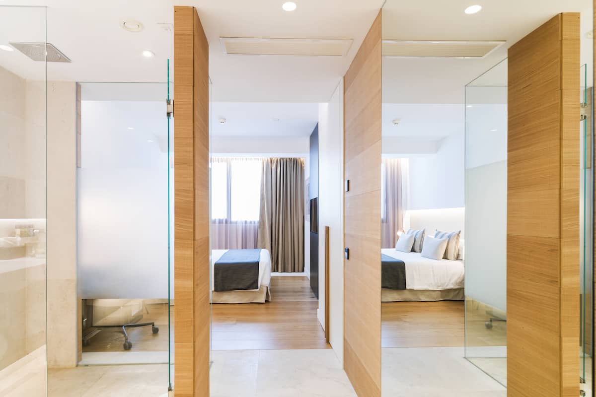 Een moderne hotelkamer met een glazen scheiding, een houten garderobe, een bed met wit beddengoed en een douchehoek.