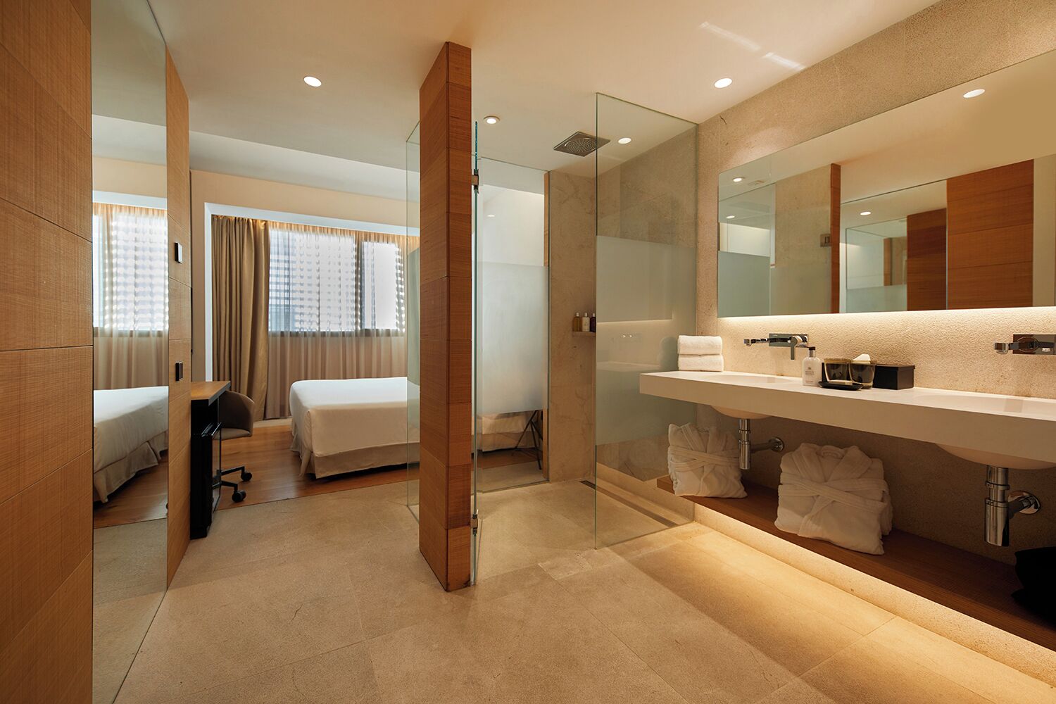 A modern hotel room with a large bed, a separate bathroom with a glass shower enclosure, and a vanity with a mirror and toiletries.