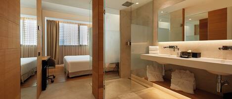A modern hotel room with a large bed, a separate bathroom with a glass shower enclosure, and a vanity with a mirror and toiletries.