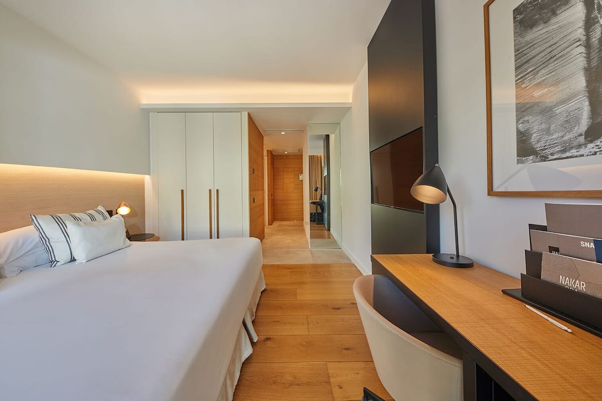 Een moderne hotelkamer met een groot bed, een bureau met lamp, een televisie en een ingelijste afbeelding aan de muur.