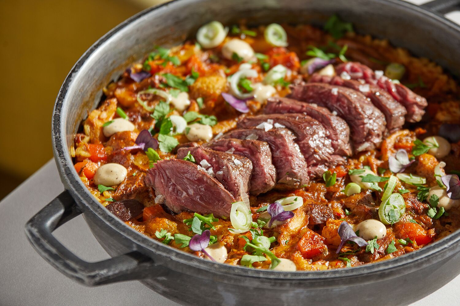 Una olla grande llena de un guiso, adornado con hierbas y trozos de carne.