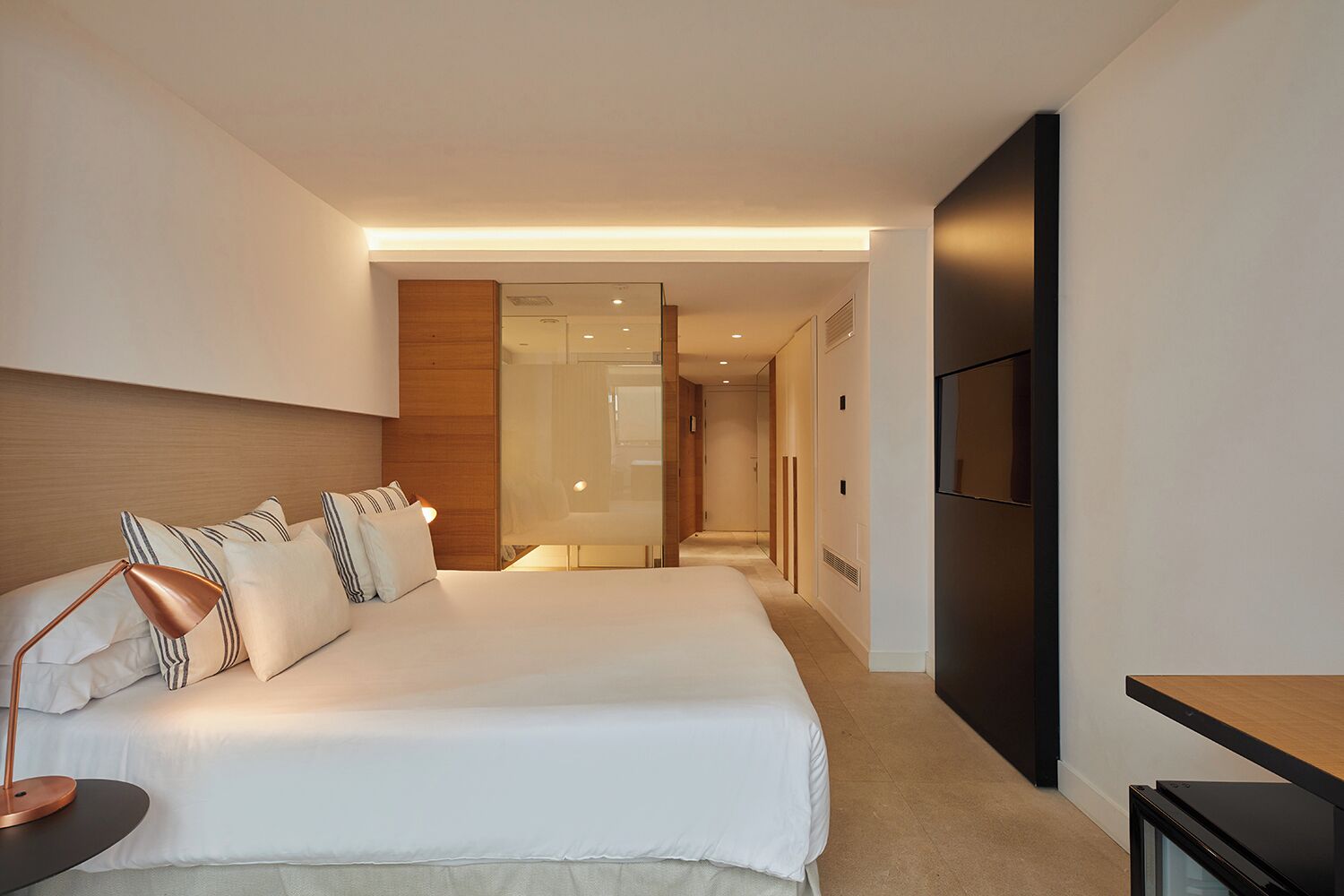 A modern hotel room with a large bed, a bedside lamp, a flat-screen TV, and a walk-in closet.