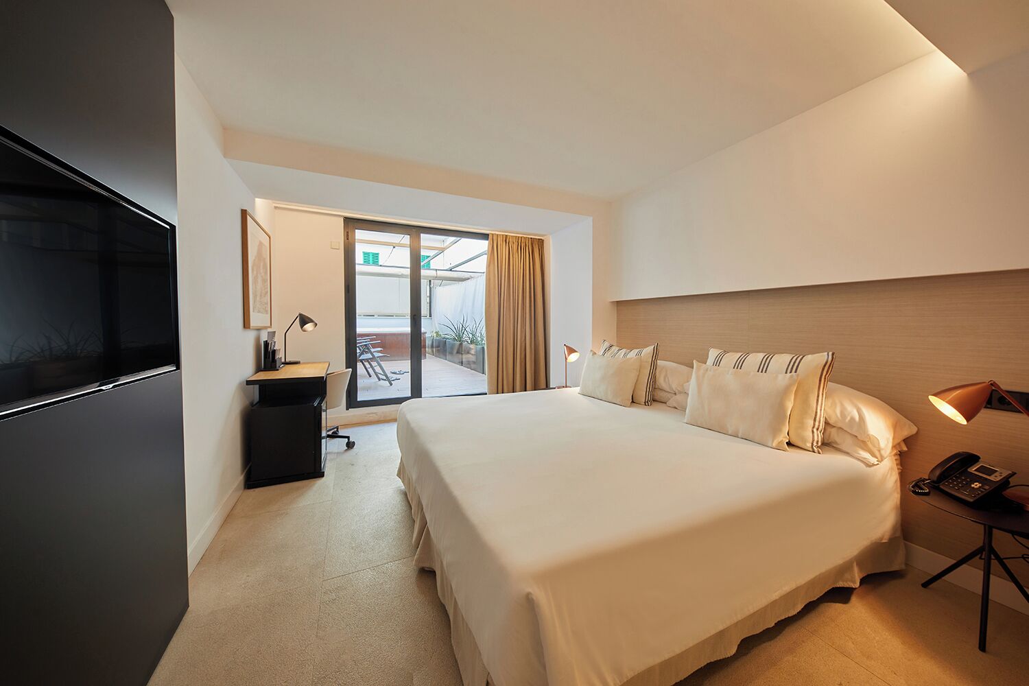 Une chambre d’hôtel avec un grand lit, un bureau, une chaise, une télévision et une porte-fenêtre coulissante donnant sur l’extérieur.