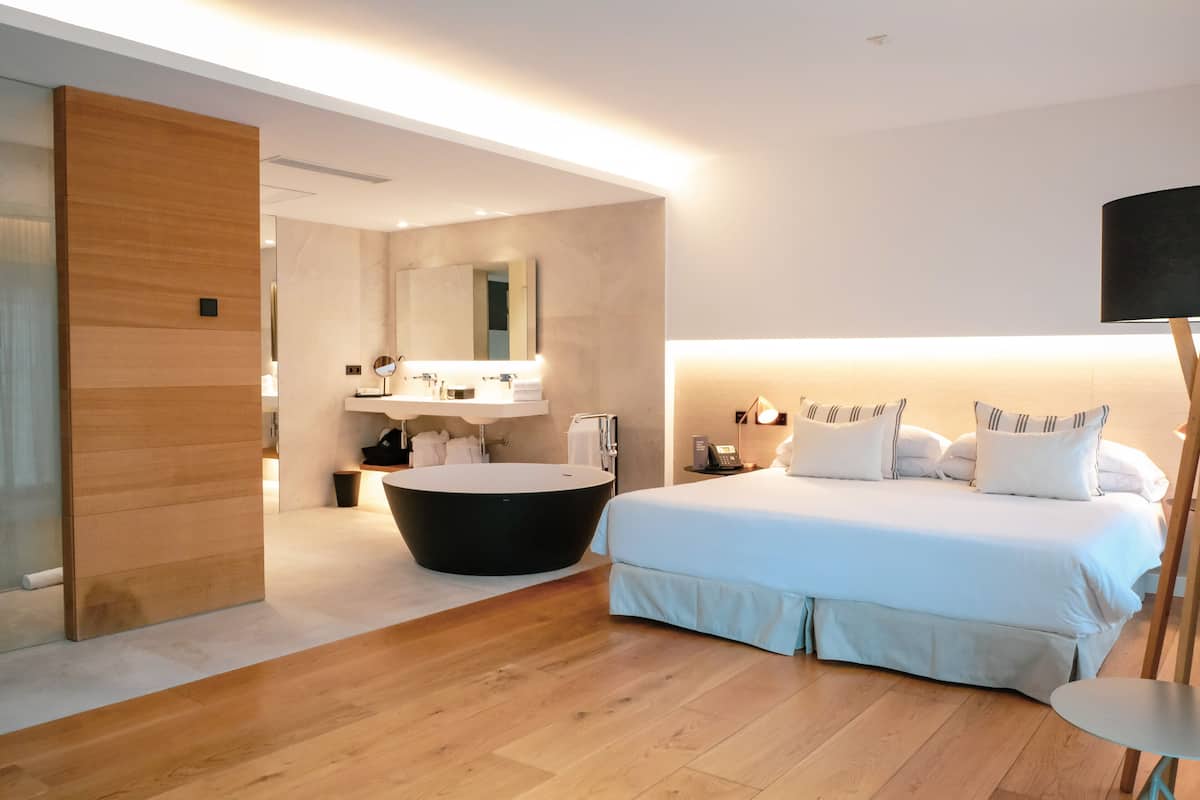 Een moderne slaapkamer met een groot bed, een rond ligbad en een houten vloer.
