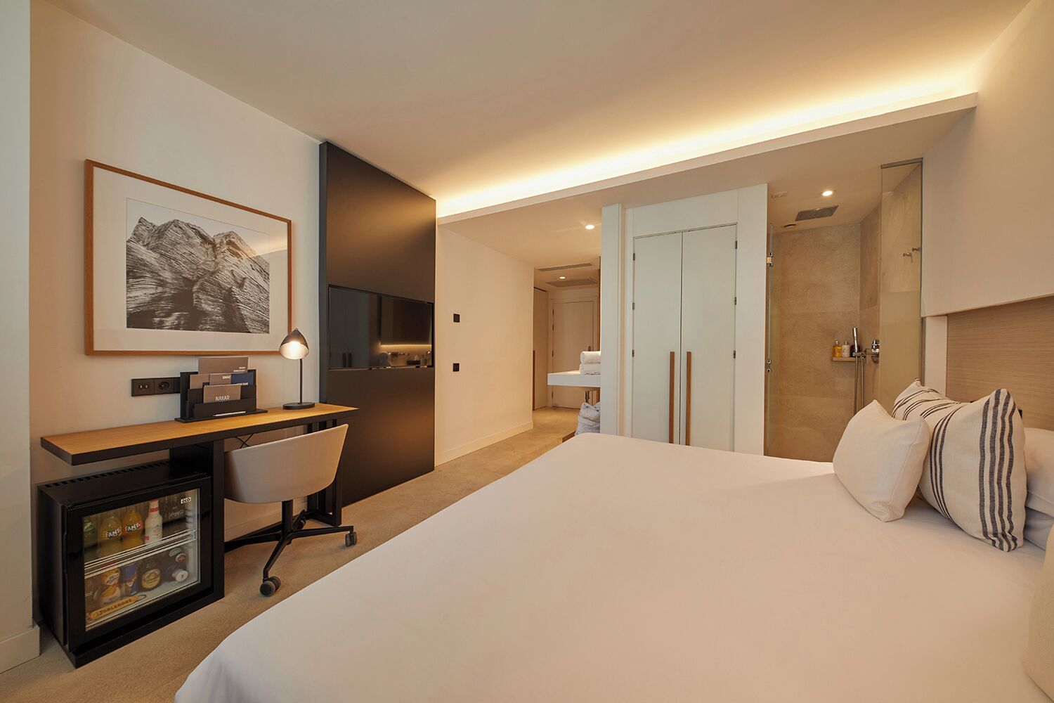 Hotelkamer met een bed, bureau met stoel, minibar, een ingelijste foto aan de muur en een kledingkast.
