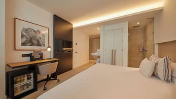 A hotel room with a bed, a desk with a chair, a minibar, a framed picture on the wall, and a wardrobe.