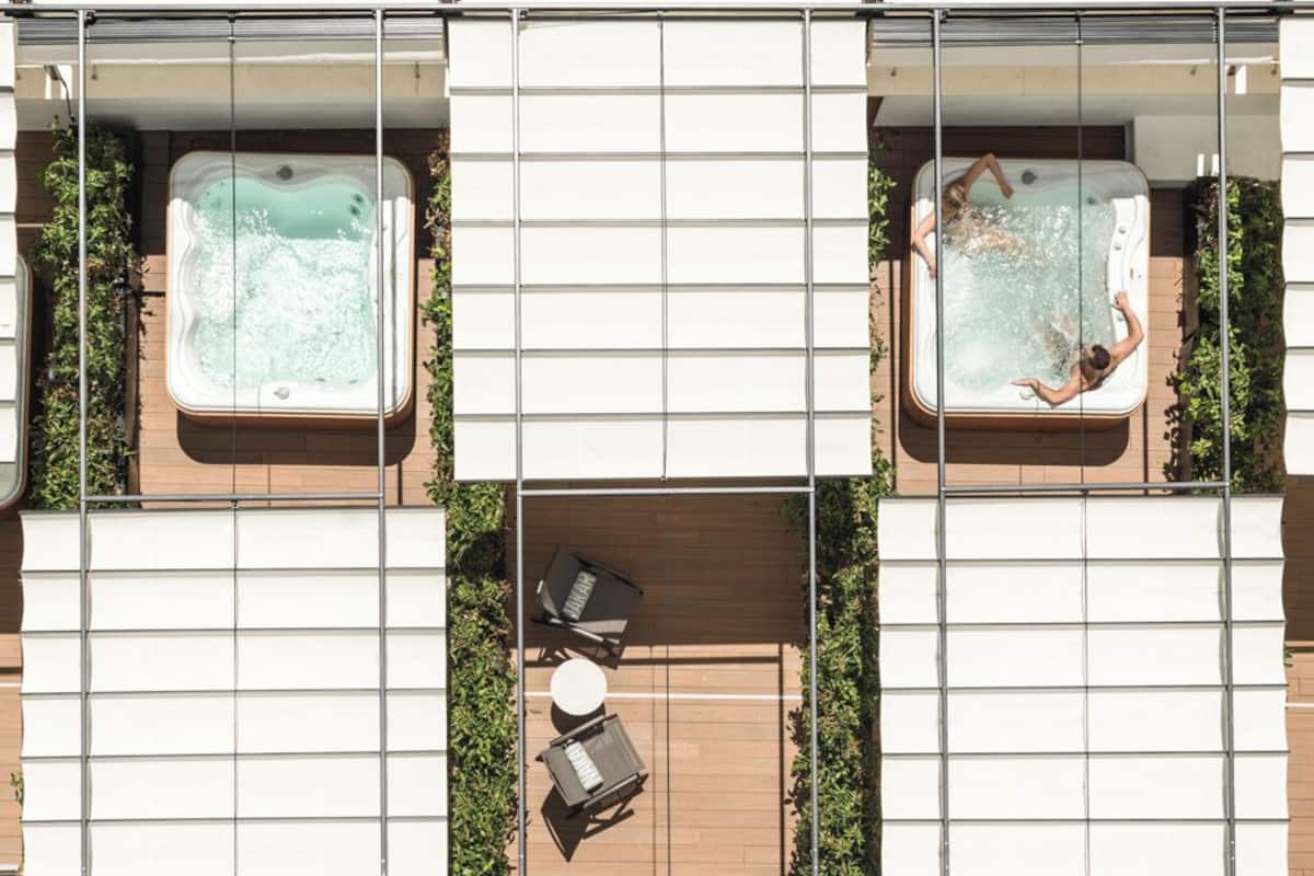 Een terras op het dak met twee jacuzzi's, omringd door zitgedeeltes en een metalen hekwerk.