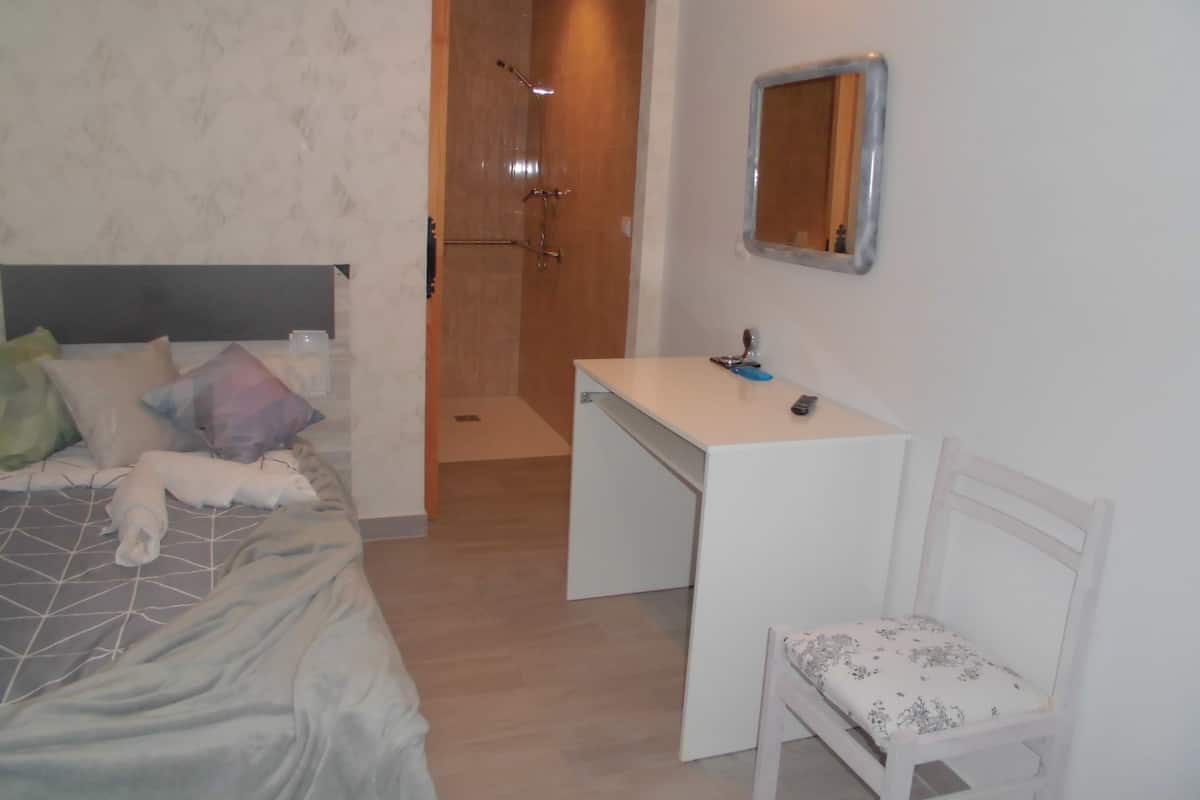 Een slaapkamer met een bed, een bureau, een stoel, een douche en een spiegel.