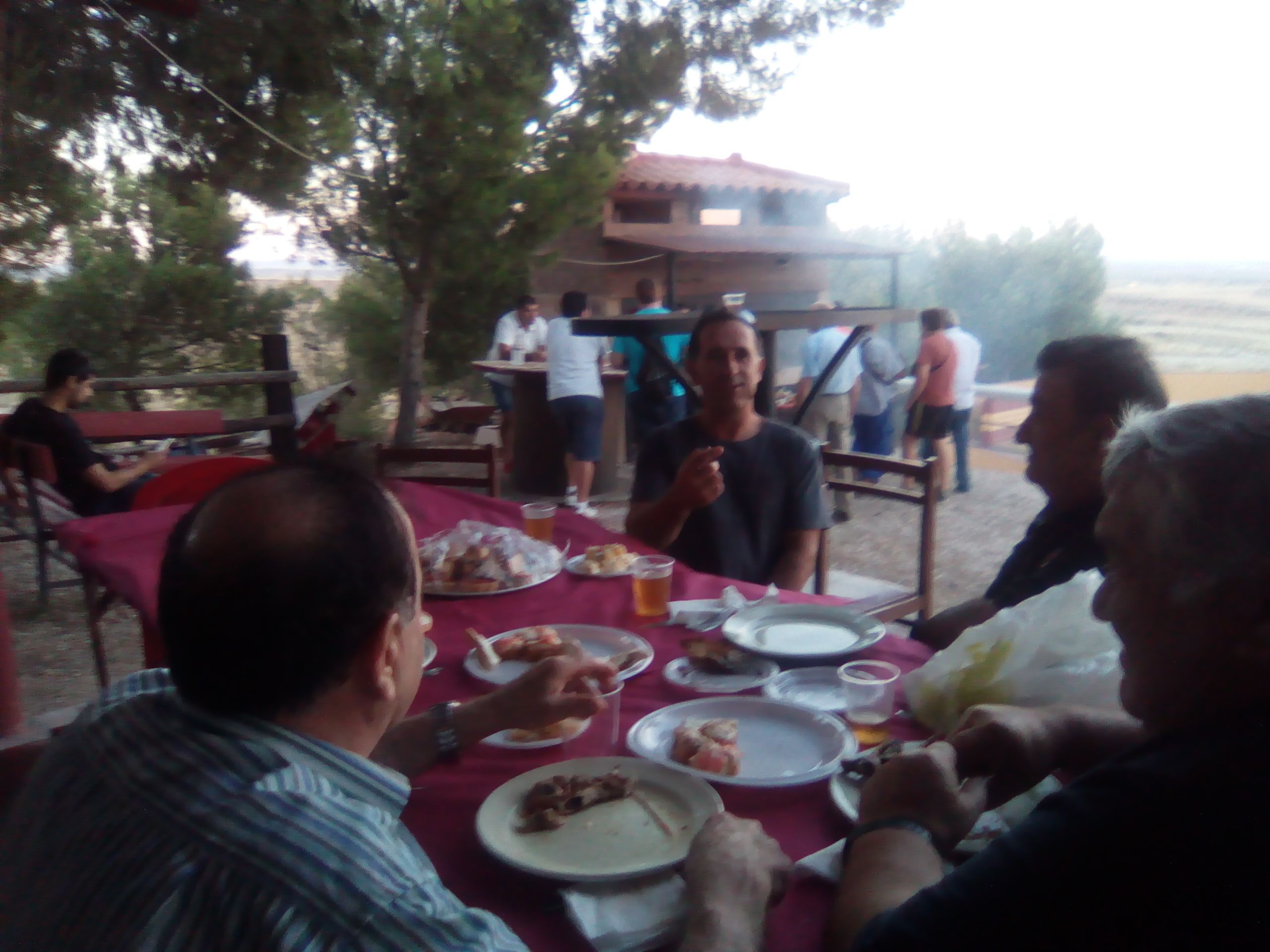 Un grupo de personas cenando al aire libre en una mesa con platos de comida y bebidas.