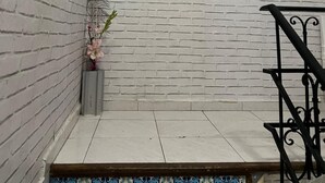 Una escalera con un muro de ladrillo blanco, un cuadro de un hombre y una mujer junto a una mesa, y una barandilla de metal.