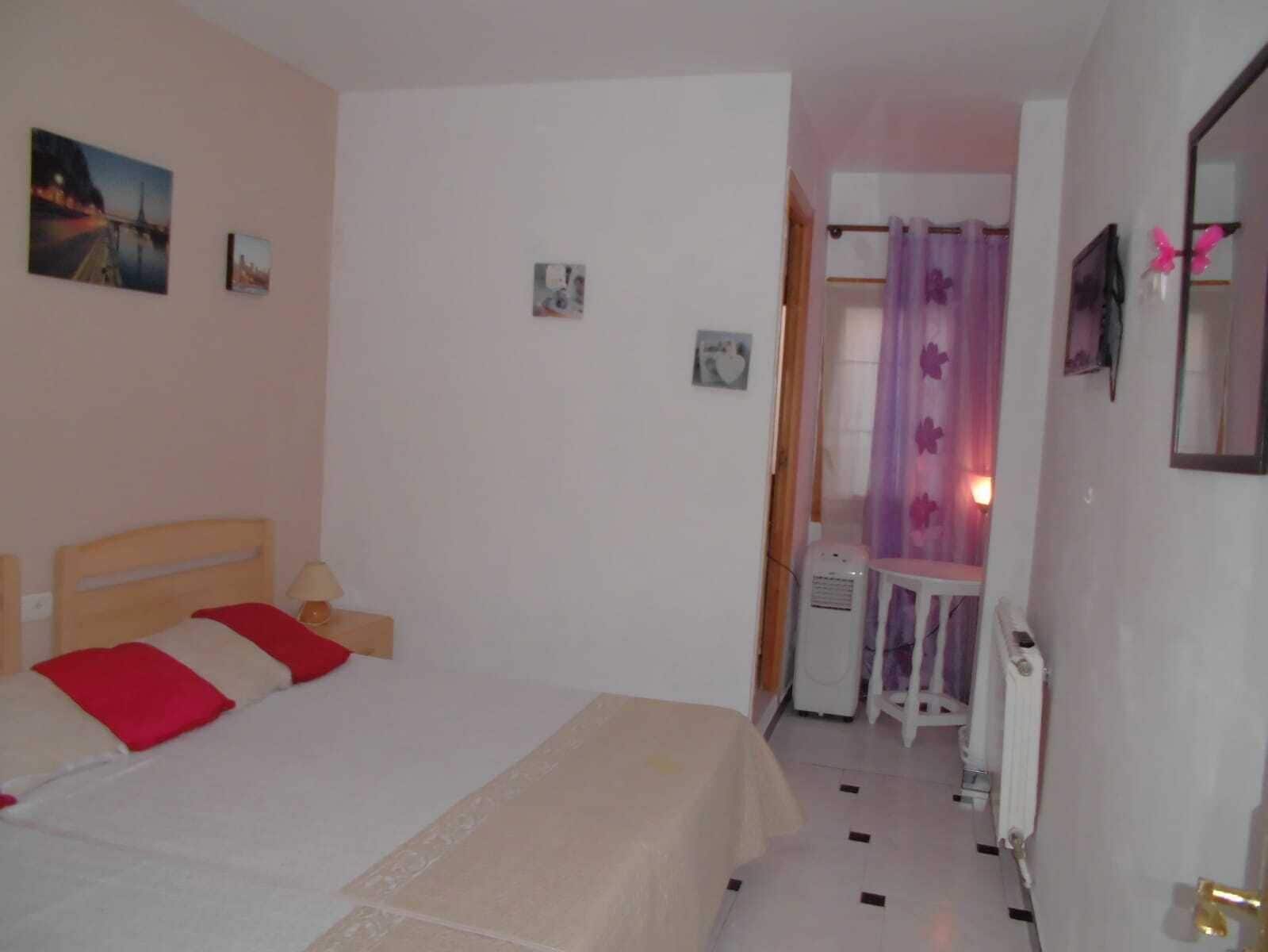 Een slaapkamer met een bed, een tafeltje, een radiator en een deur naar een andere kamer.