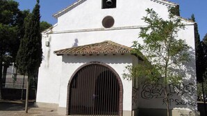 Un edificio blanco con una torre de campanas, una entrada arqueada grande y grafitis en la pared.