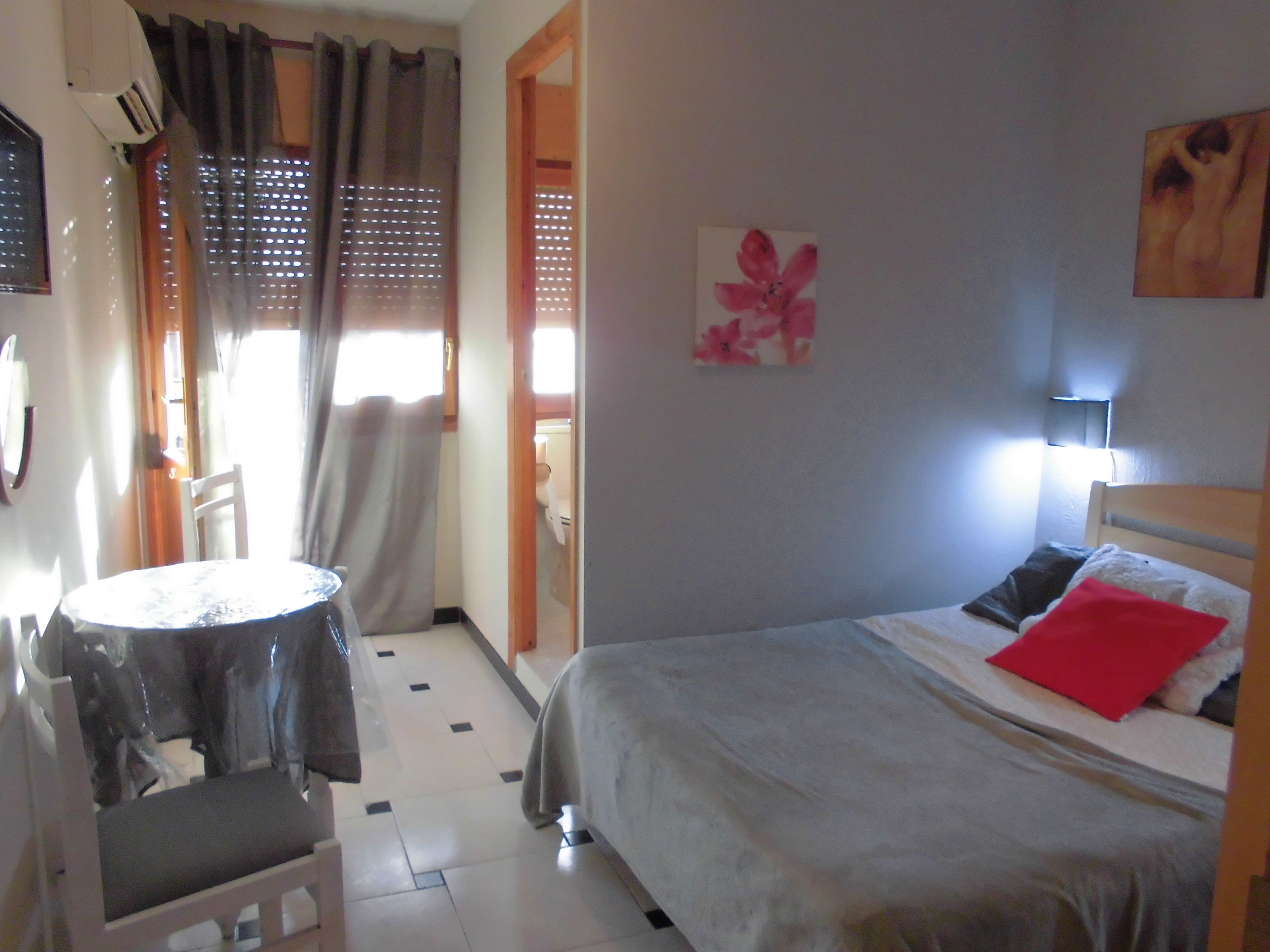 A bedroom with a bed, a chair, a table, and a window with curtains.