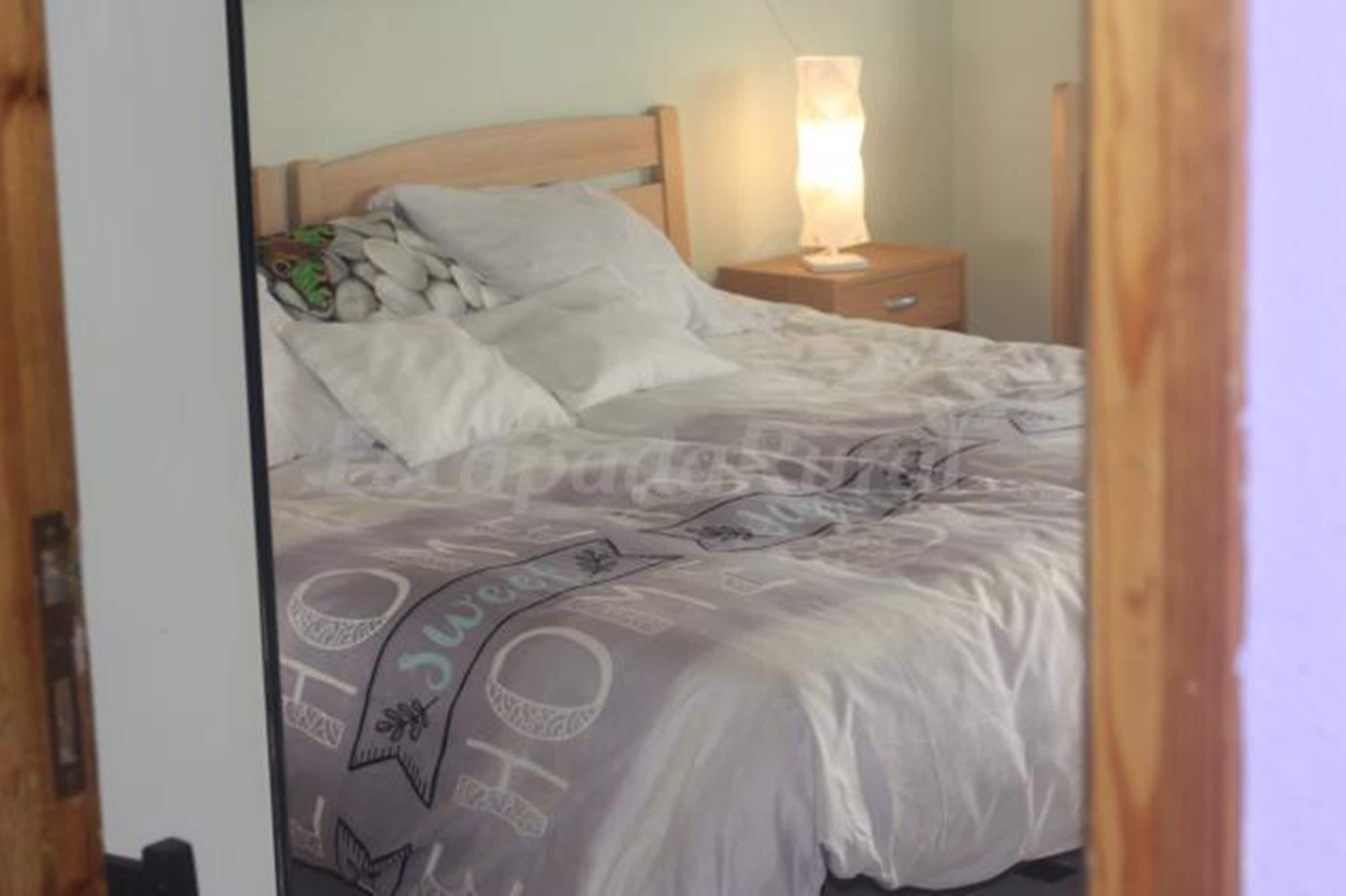 Un dormitorio con cama, almohadas, una mesita de noche con lámpara y cabecero de madera.