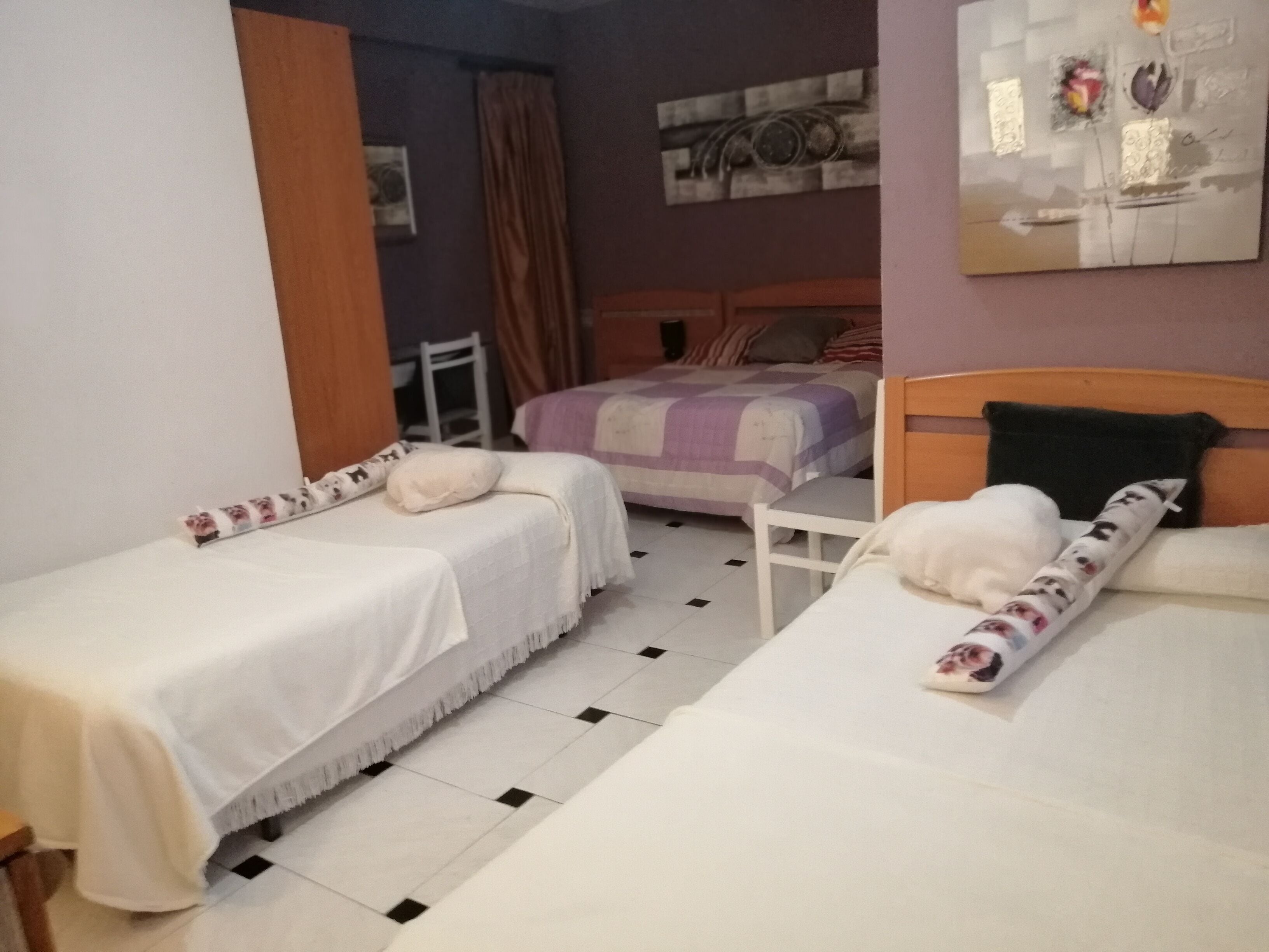 A hotel room with two single beds, a wooden headboard, a small table, and a chair.